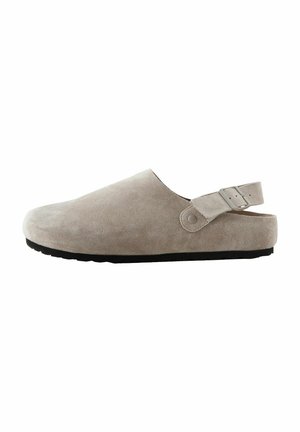 Sabot en daim gris clair à enfiler avec une sangle arrière, doté d'un bout rond et d'une semelle texturée pour une meilleure adhérence. Accentué par un détail de bouton-pression.