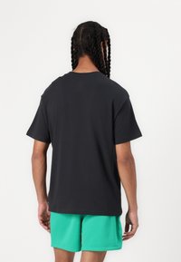 Camiseta de algodón negra de manga corta y cuello redondo, combinada con pantalones cortos verdes, mostrando un ajuste relajado y una textura suave.