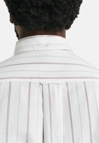 Camisa blanca con rayas verticales rojas y azules, con cuello clásico y un solo botón en la parte posterior del cuello, fabricada en algodón texturizado.