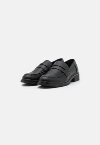 Black leather loafers with a low block heel, featuring two decorative straps and stitching details along the rounded toe and sides.