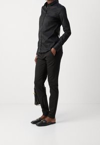 Svart skjorta med knappar i kombination med skräddarsydda svarta byxor och svarta loafers med gulddetaljer. Slät tyg och figursydd design.