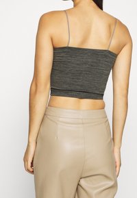 Top corto grigio a coste con spalline sottili regolabili, abbinato a pantaloni beige a vita alta. Tessuto liscio e design aderente.