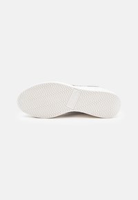 White sneaker outsole with a zigzag tread pattern, featuring a rectangular logo plate. Smooth rubber material with a matte finish.