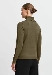 Olivgrön stickad polotröja med långa ärmar, ribbat avslut och avslappnad passform, som visar en slät textur och minimal detaljer.