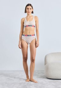 Λευκό εσώρουχο με δαντέλα και ταιριαστά εσώρουχα με λωρίδα "DIESEL" σε μαύρο και κόκκινο χρώμα; εφαρμοστό σχέδιο, ελαστικό υλικό και λουλουδάτη όψη.