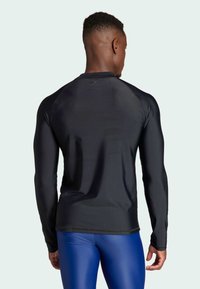 Maglietta atletica nera a maniche lunghe con una texture liscia, caratterizzata da un collo rotondo e un design aderente. Cuciture visibili sulle spalle.