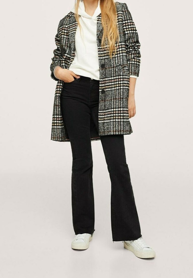 Cappotto in misto lana con un motivo a quadri bianco e nero, con una vestibilità su misura e due bottoni, abbinato a pantaloni neri a palazzo e sneakers bianche.