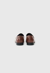 Brown leather dress shoes with a smooth texture, low heel, and minimalistic design. Black rubber sole with logo detail on the heel.