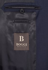 Notranjost mornarskega blejzerja z gladkim, satinastim podlogom, žepom s poklopcem in rjavim etiketom z belim vtisnjenim "B" in "BOGGI MILANO."