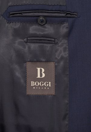 Navy blazerin sisäosa, jossa on sileä, satiininen vuori, läppätasku ja ruskea etiketti, jossa on valkoinen kohokuvioitu "B" ja "BOGGI MILANO."