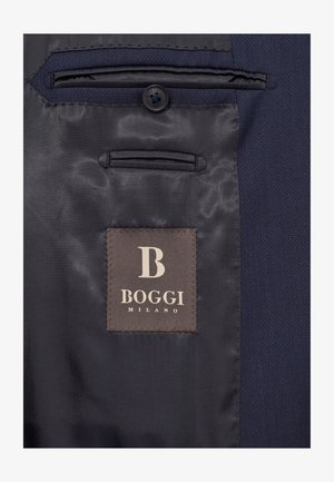 Navy blazerin sisäosa, jossa on sileä, satiininen vuori, läppätasku ja ruskea etiketti, jossa on valkoinen kohokuvioitu "B" ja "BOGGI MILANO."