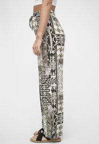 Svarte og kremfargede bukser med brede ben, snøring i midjen og en avslappet passform, med intrikate blomster- og geometriske mønstre.