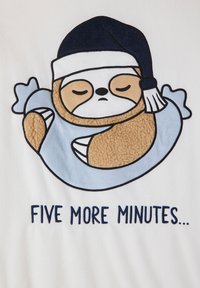 Illustrazione di un bradipo addormentato in un sacco a pelo blu con un berretto blu scuro, ricamato su un tessuto bianco. Il testo recita "ANCHE CINQUE MINUTI..."