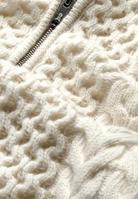Crème-kleurige gebreide trui met een gestructureerd patroon, voorzien van een rits aan de voorkant, met opvallende kabel- en ribbelontwerpen.