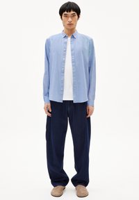 Light blue button-up shirt, long sleeves, with a classic collar, paired with dark navy wide-leg pants and beige slip-on footwear.