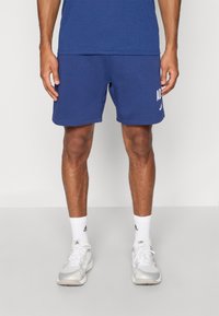 Blauwe sportshorts van zacht materiaal met een wit logodetail aan de linkerkant. Voorzien van een elastische tailleband en een klassiek model.