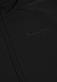 Felpa nera con zip caratterizzata da una texture a costine e un logo "Champion" goffrato in modo sottile sul petto. Realizzata in un materiale liscio e elastico.