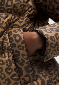 Přesná bunda s leopardím potiskem v hnědých tónech s černými akcenty. Texturovaná látka s viditelnou rukou v kapse. Detaily zahrnují prošívaný design.