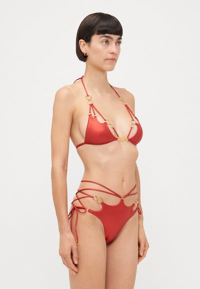 Red bikini featuring a triangular top with gold ring accents and thin adjustable straps, and bottoms with crisscross detailing and rings.