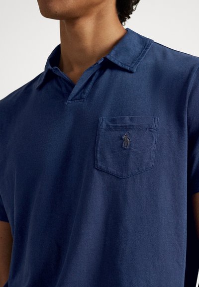 Polo azul-marinho com colarinho, textura do tecido visível, apresentando um bolso no peito e logótipo bordado na mesma cor.