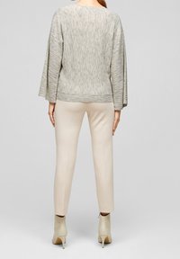 Light gray, textured long-sleeve top with a rounded neckline and a loose fit, paired with beige tailored pants and cream-colored heeled booties.