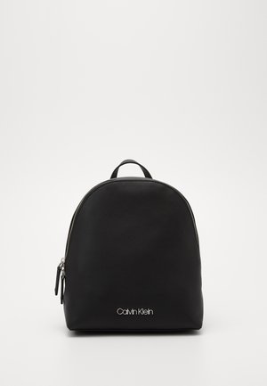 Mały czarny plecak Calvin Klein z srebrnym zamkiem błyskawicznym i logo z przodu, na jednolitym białym tle.