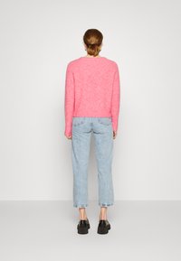 Rosa flauschiger Pullover mit rundem Halsausschnitt, kombiniert mit hellblauen geraden Jeans. Sichtbare schwarze Schuhe mit dicker Sohle. Rückansicht.