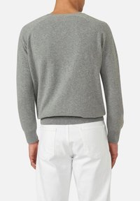 Grauer gestrickter Pullover mit geripptem Saum und Bündchen, mit einem klassischen Rundhalsausschnitt. Kombiniert mit weißen Jeans, von hinten gesehen.