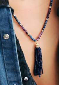 Collier en perles présentant des perles violettes et bleues, des accents dorés et un long pendentif en forme de frange bleue.