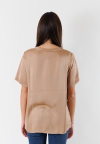 Blusa beige a maniche corte realizzata in materiale morbido, con scollatura tonda e vestibilità comoda, con orlo posteriore leggermente più lungo.