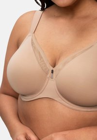 Sujetador beige con copas lisas, detalles de malla en la parte superior, tirantes ajustables y un cierre de gancho en el frente. Textura suave y forma redondeada.