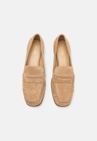 Beige suède instappers met een afgeronde neus, gestikte details en een glad leren binnenzool. Minimalistisch ontwerp zonder hardware accenten.
