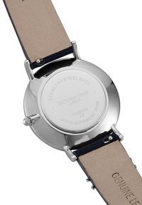 Fond de montre en acier inoxydable avec gravure de la marque et des détails du mouvement. Bracelet en cuir avec un dessous beige et un dessus bleu foncé. Matériel réglable.