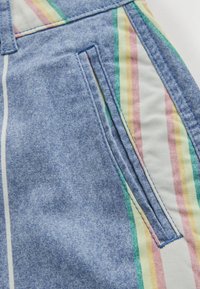 Gros plan d'une poche en tissu denim bleu avec des rayures verticales colorées en jaune pastel, rose, vert et blanc sur la couture latérale.