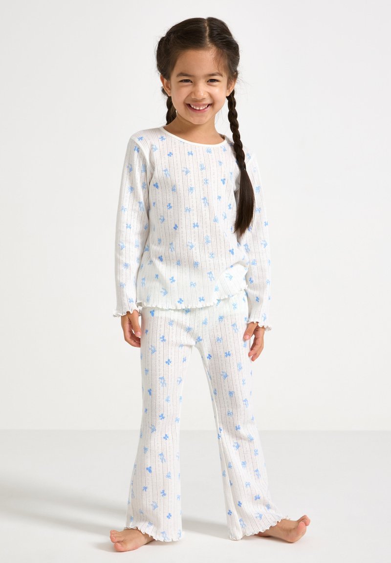 Ensemble de pyjama en coton avec une base blanche ornée de motifs floraux bleus, texture côtelée, manches longues et pantalons évasés avec des ourlets festonnés.