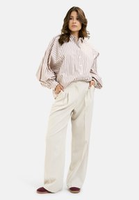 Striped oversized shirt in cream and beige, paired with loose cream trousers and maroon slip-on shoes, showcasing soft fabric and relaxed fit.