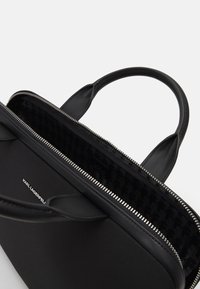 Sort håndtaske med en glat yderside og to top-hanke. Har lynlåslukning og et mønstret stoffor indvendigt.