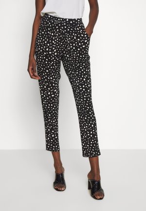 Czarne, zwężane spodnie z wysokim stanem w biały nieregularny wzór kropek, noszone z białym topem i czarnymi, odkrytymi na palcach sandałami na obcasie z srebrnymi ćwiekami.