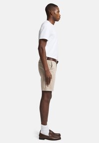 Hvid kortærmet t-shirt, khaki shorts, brune læder loafers, hvide sokker. Profilvisning der viser en afslappet pasform og rene linjer.