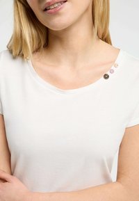Camicia bianca a maniche corte con scollatura a girocollo. Presenta quattro bottoni decorativi di diversi colori lungo la cucitura della spalla. Tessuto morbido.