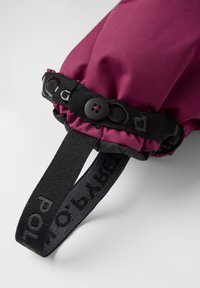 Violetti kangaskäsi, jossa on musta säädettävä hihna, napilla suljettuna ja teksturoiduilla yksityiskohdilla, kiinnitettynä sileään mustaan hihnaan.