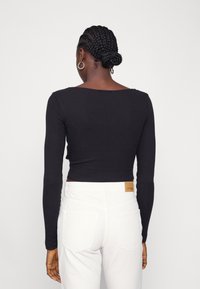 Top preto de manga longa com decote quadrado, design ajustado e tecido texturizado, combinado com jeans brancos de cintura alta com bolsos traseiros.