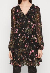 Musta kukallinen pitkähihaista mekkoa, jossa on vaaleanpunaisia, punaisia ja vihreitä kukkakuoseja, läpinäkyvät hihat, ripsutetut V-pääntie ja kerroksellinen helma.