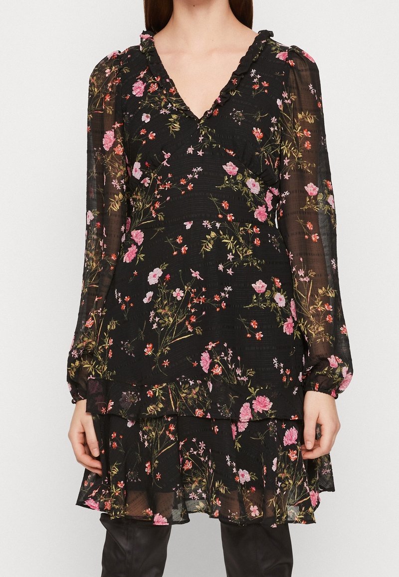 Musta kukallinen pitkähihaista mekkoa, jossa on vaaleanpunaisia, punaisia ja vihreitä kukkakuoseja, läpinäkyvät hihat, ripsutetut V-pääntie ja kerroksellinen helma.