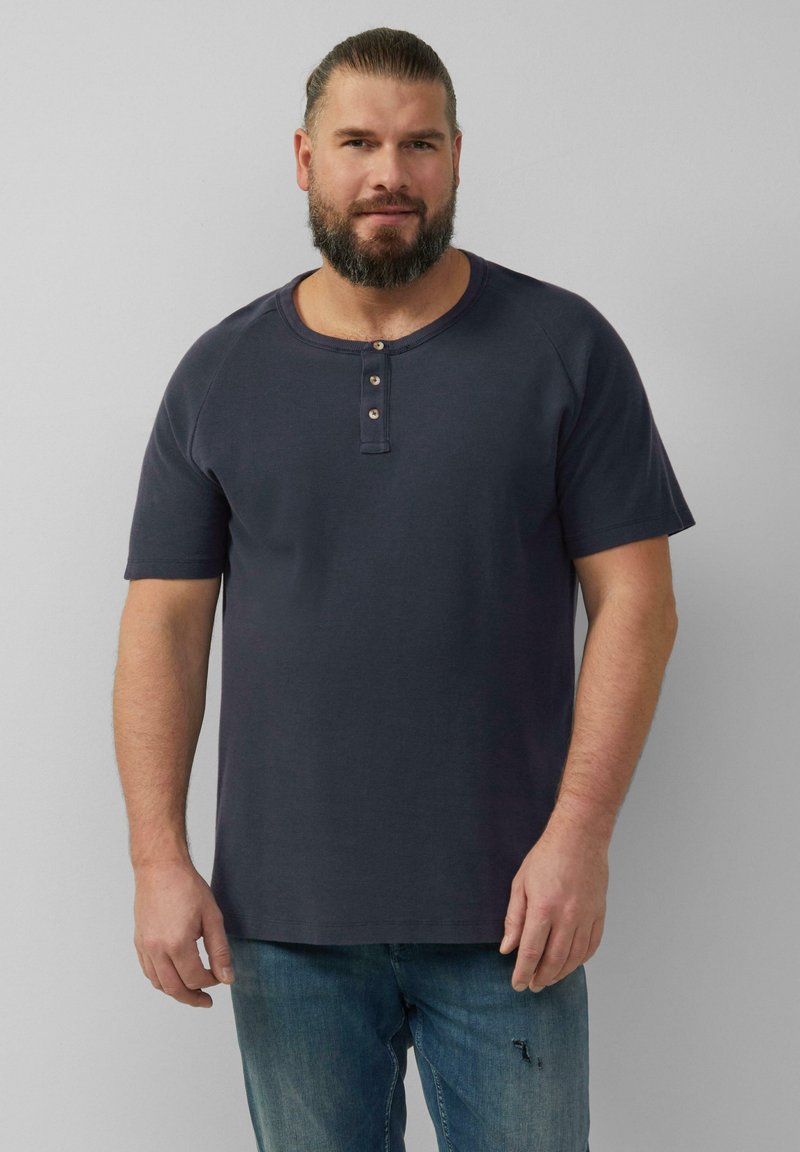 Granatowy t-shirt henley z krótkim rękawem z trzema drewnianymi guzikami przy dekolcie, zestawiony z wyblakłymi niebieskimi dżinsami w luźnym kroju.