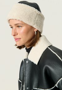 Svart läderjacka med krämfärgad faux shearling-krage och manschetter; krämfärgad shearlinghatt; elegant design, minimala accenter och mjuka texturer.