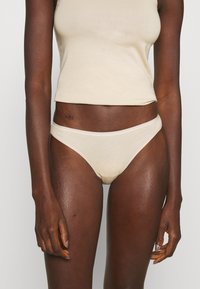 Beige Baumwoll-Top und passende Unterwäsche im Bikini-Stil. Weicher Stoff, minimale Nähte, glatte Textur und tief sitzendes Design.
