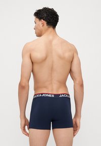 Marinblå bomullsboxershorts med en vit och röd märkeselastic, figursydd design och en slät textur, sedd bakifrån.