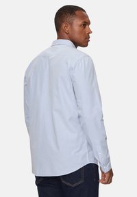 Camicia button-up azzurro chiaro con colletto classico, maniche lunghe e fondo curvo; tessuto in cotone con una texture liscia e dettagli minimi.