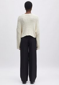 Gemütlicher, verkürzter weißer Strickpullover mit strukturiertem Muster, kombiniert mit hochtaillierten, weit geschnittenen schwarzen Hosen.